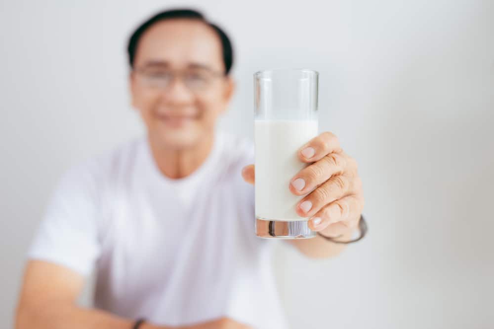 Молоко мужчинам после 50. Young Asian man pouring Milk into measuring Cup.